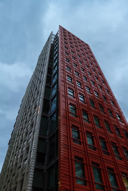 This image features two modern high-rise buildings; one in red and one in grey, reaching towards a cloudy sky. It captures contemporary urban design and can be used for topics related to architecture, city life, urban development, and modern office spaces.