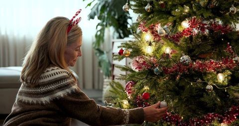 Woman Decorating Christmas Tree with Baubles and Festive Antler Headband