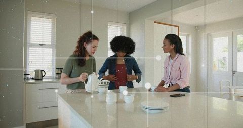 Pouring tea and chatting, three women gathered at modern kitchen island for casual morning