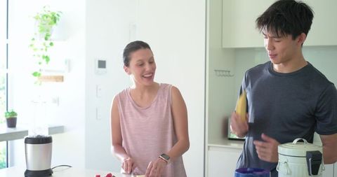 Diverse couple chopping strawberries and preparing smoothie on sunlit kitchen island