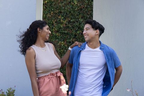 Laughing african american couple enjoying casual moment in courtyard with green hedge