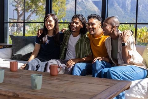 Diverse friends laughing and relaxing on sofa in sunny modern living room