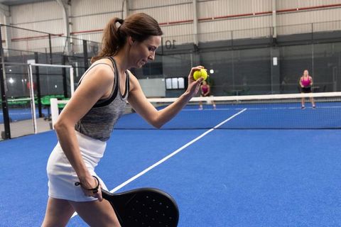 Female athlete serving pickleball on indoor blue court with paddle and yellow ball