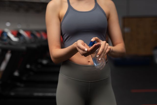 Caucasian woman applying hand sanitizer in gym, promoting hygiene and safety during workouts. Ideal for articles on fitness, health, and virus prevention. Useful for gym advertisements, health blogs, and hygiene awareness campaigns.