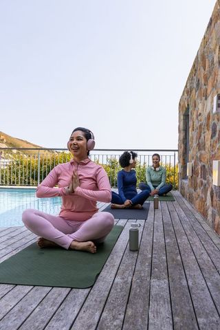 Multicultural women practicing yoga on poolside deck during outdoor mindfulness session