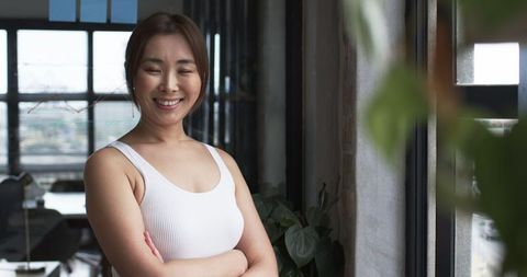 Asian Woman Exuding Confidence in Modern Office with Crossed Arms