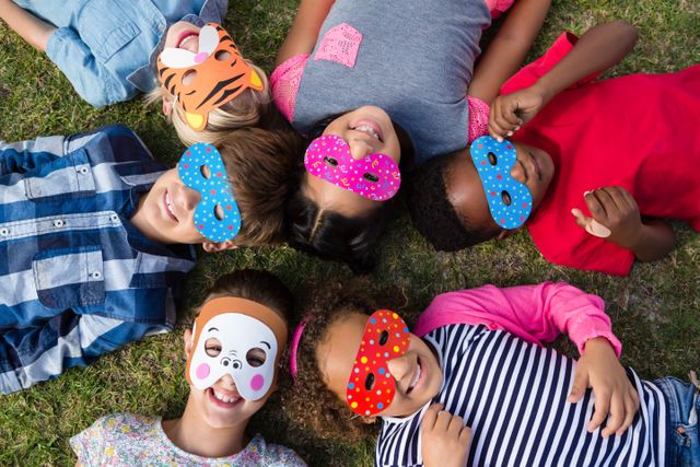 Directly above shot of children wearing masks while lying on field in yard