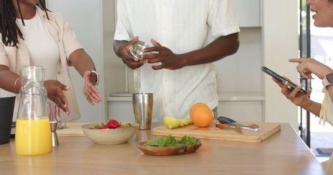 Friends mixing cocktails with phone ar guidance on bright kitchen island, daytime