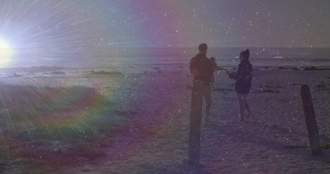 Couple walking on beach at sunset holding baby with dramatic sun flare