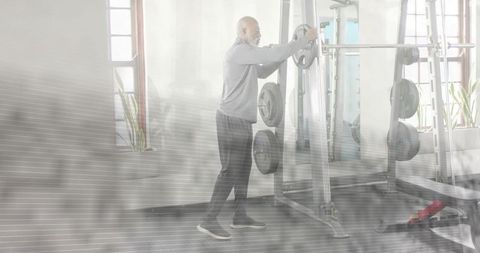 Mature man adjusting weight plate on barbell at squat rack for strength training