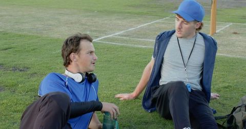 Coach and player discussing strategy while resting on grass during practice break with whistle