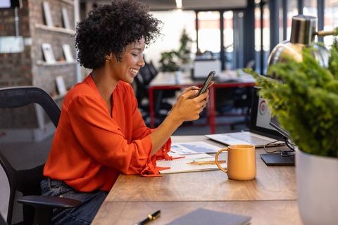 African American Woman Reviewing Charts on Smartphone in Modern Office