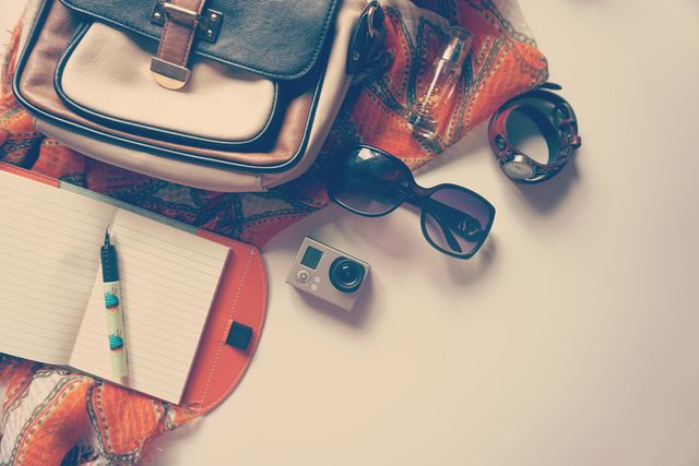 Essential travel items including a backpack, sunglasses, camera, notebook, scarf, and watch are arranged on a desk. Perfect for illustrating travel planning, vacation preparations, or adventure lifestyle themes. Useful for blogs, travel websites, packing guides, or promotional material for travel products.