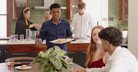 Diverse friends gathering in modern kitchen serving snacks and chatting at dinner party