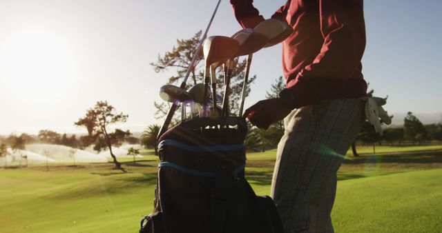 Man adjusting golf clubs in a bag on a bright sunny day at a golf course. Ideal for promoting golfing events, sports equipment, or leisure activities. Great for websites, brochure designs, advertising golf resorts, or articles about outdoor sports and hobbies.