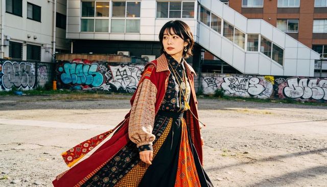 Walking asian woman wearing layered patterned streetwear crossing urban lot with graffiti