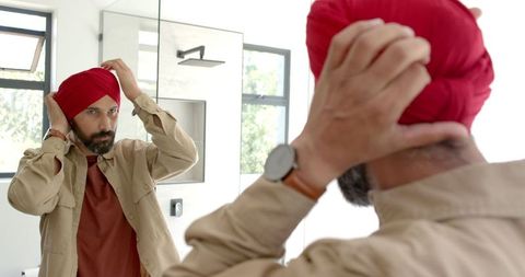 Man adjusting red turban in mirror