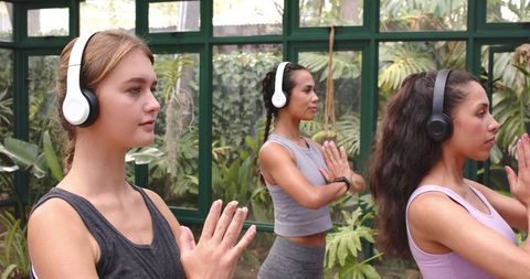 Women Meditating with Headphones in Bright Glasshouse Studio