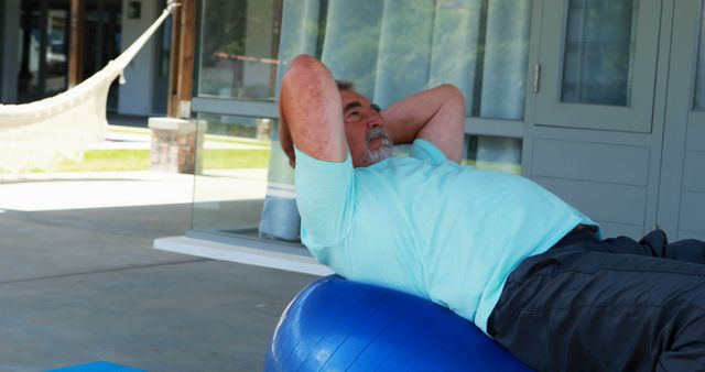 A middle-aged man is exercising on a blue fitness ball in a home patio area, with copy space - Download Free Stock Photos Pikwizard.com