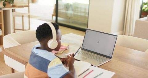 Child learning remotely with headphones at modern home workspace and laptop