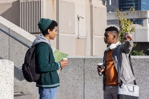 Diverse college students talking on urban campus holding coffee, backpack and notebooks