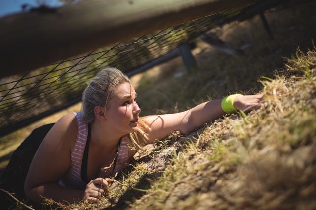 Determined woman crawling under the net during obstacle course in boot camp
