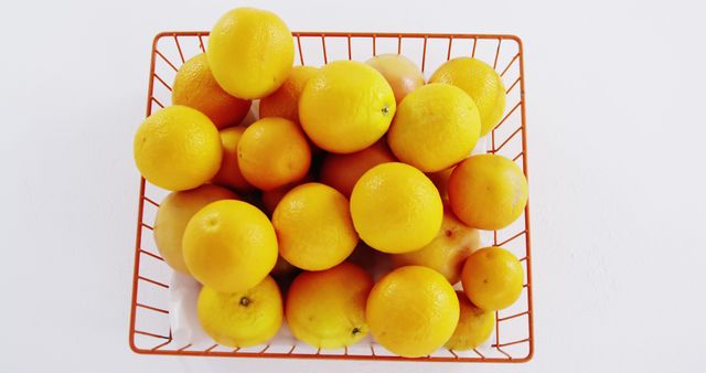 Bright fresh oranges fill a wire basket, placed against a white background. Use this image for health and nutrition blogs, food photography, fresh produce advertisements, or kitchen decor.