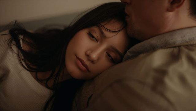 Resting woman leaning on partner shoulder in warm low light, intimate cozy couple moment