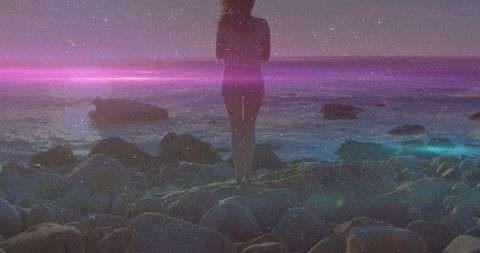 Woman in Swimsuit Rocks by Shoreline at Dusk with Lens Flare