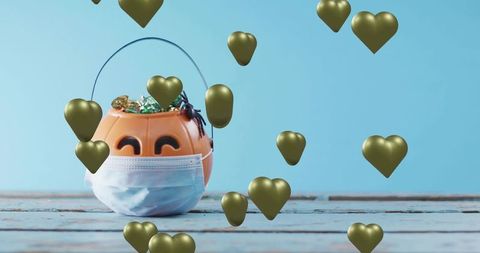 Jack-o'-lantern wearing surgical mask on candy bucket with floating gold hearts, Halloween safety