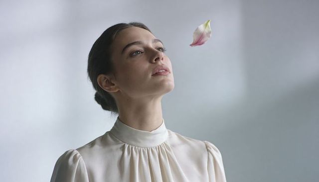 Graceful woman gazing upward with floating flower petal, minimalist serene portrait