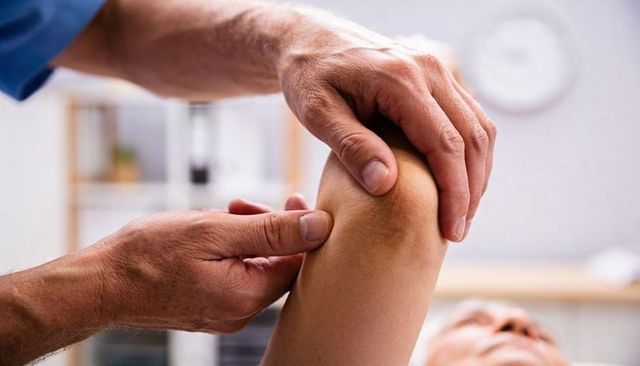 Physiotherapist manipulating knee joint during manual therapy consultation in clinic