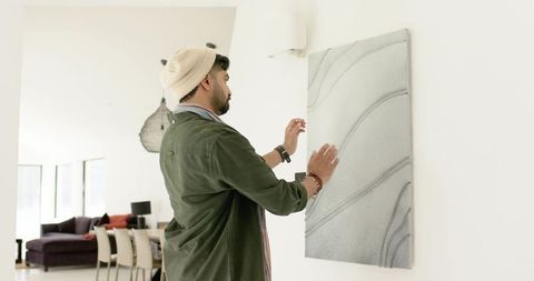 Indian man adjusting abstract wall panel in modern open-plan living space, minimalist decor