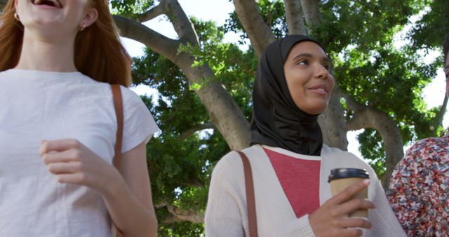 A group of diverse friends, including a woman in hijab, walking outdoors on a sunny day, smiling and enjoying themselves. Use this for depicting diversity, friendship, summer activities, or casual outings.