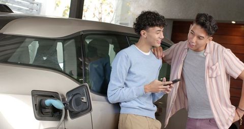 Diverse friends discussing next to electric car in garage