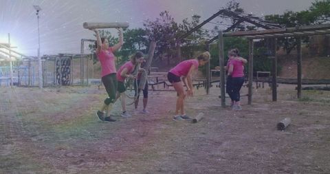 Women in outdoor fitness challenge carry logs on obstacle course