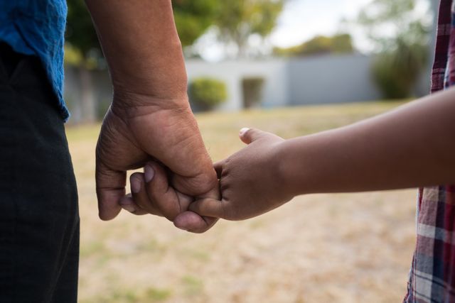 Close up of grandfather and grandson holding fingers while standing in yard