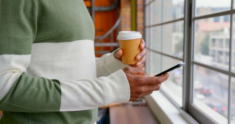 Businessman Holding Coffee and Phone by Office Window
