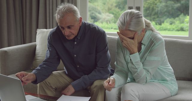Senior Caucasian couple reviews documents at home, with copy space. They appear concerned while analyzing financial papers.
