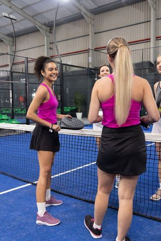 Female padel players gathering at net on indoor blue court smiling team moment