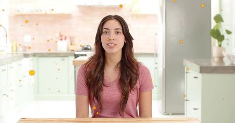 Young woman speaking to camera while sitting at pastel kitchen table, lifestyle portrait