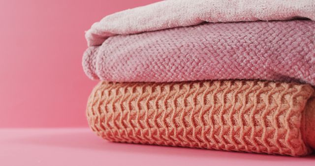 Image of folded blankets lying on pink background. fabrics, textiles, home styling and coziness concept.