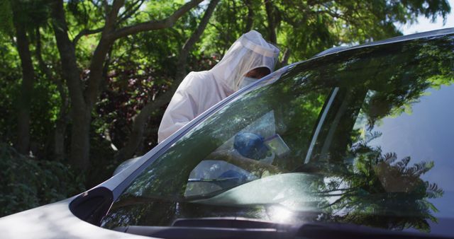 Healthcare worker in personal protective equipment is administering a drive-through COVID-19 test to a person in a car. This image is suitable for use in healthcare, pandemic response, public health campaigns, and informational materials about COVID-19 testing protocols.