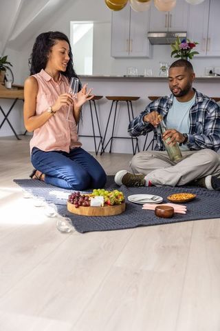 Couple enjoying indoor picnic, pouring wine and sharing charcuterie in modern kitchen