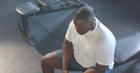 Male athlete resting on weight bench wearing headphones after intense gym session