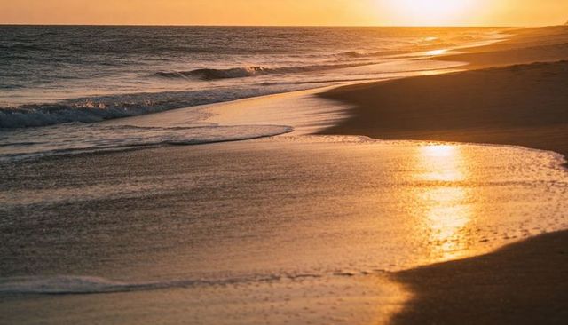 Golden sunset reflecting on wet sandy shoreline with gentle surf