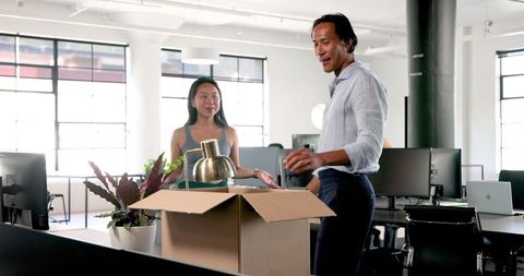 Colleagues unpacking box with office items in modern workspace