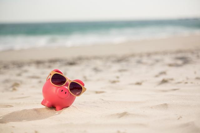 Piggy bank with sunglasses on sandy beach, representing fun and relaxation. Ideal for concepts related to summer vacations, financial savings, holiday planning, and investment. Suitable for travel agencies, financial institutions, and lifestyle blogs.