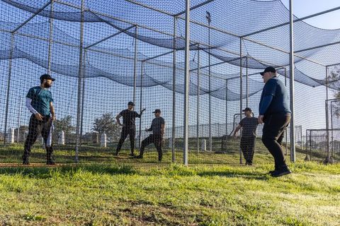 Mature baseball team practicing in netted batting cages outdoors coaching and drills