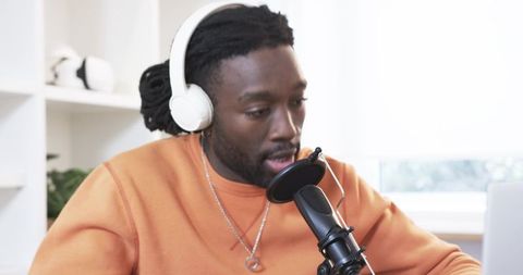 African american podcaster speaking into microphone wearing headphones in home studio